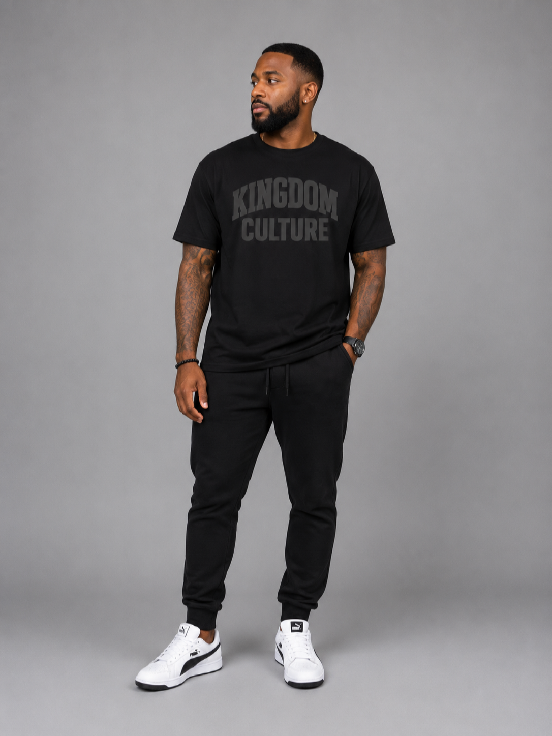 Man wearing a black 'Kingdom Culture' t-shirt and black pants on a gray background